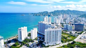 A coastal cityscape with high-rise buildings, a beach, and mountains in the background.