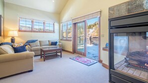 Una sala de estar acogedora con chimenea, dos sofás, una mesa de centro y ventanas amplias con vistas a un paisaje nevado.