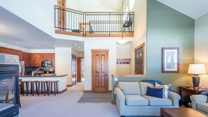 Un amplio espacio habitable con techo alto, una cocina con armarios de madera, un comedor y una escalera que sube a un nivel superior.