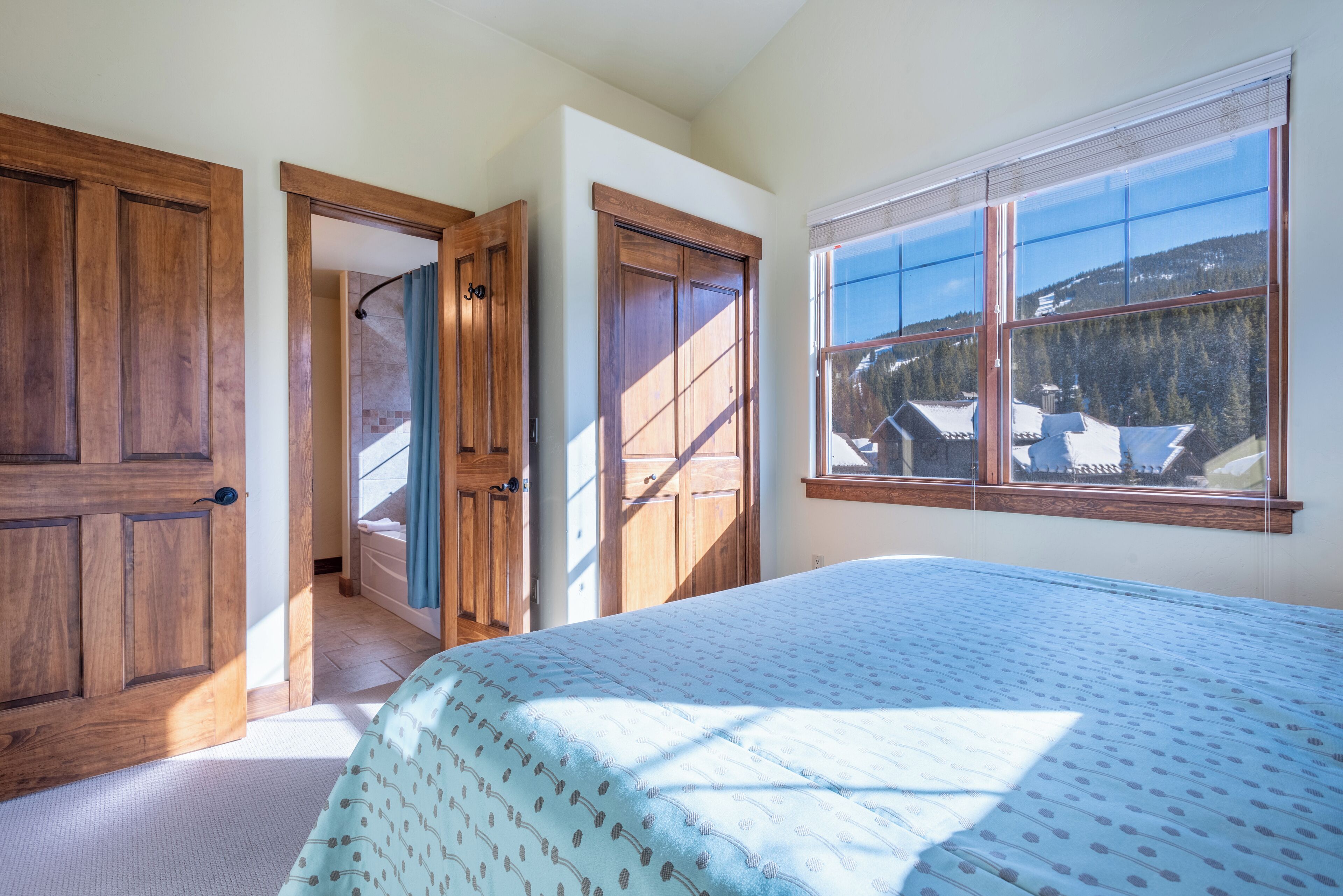 Une chambre avec un grand lit, des portes en bois et une fenêtre donnant sur une montagne.