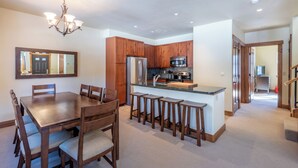 Una cocina moderna con armarios de madera, una isla central con taburetes, un refrigerador y una lámpara de araña.