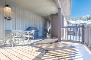 Ein überdachter Außenbereich mit Holzterrasse, Metallstühlen, einem Grill und Blick auf einen Berg.