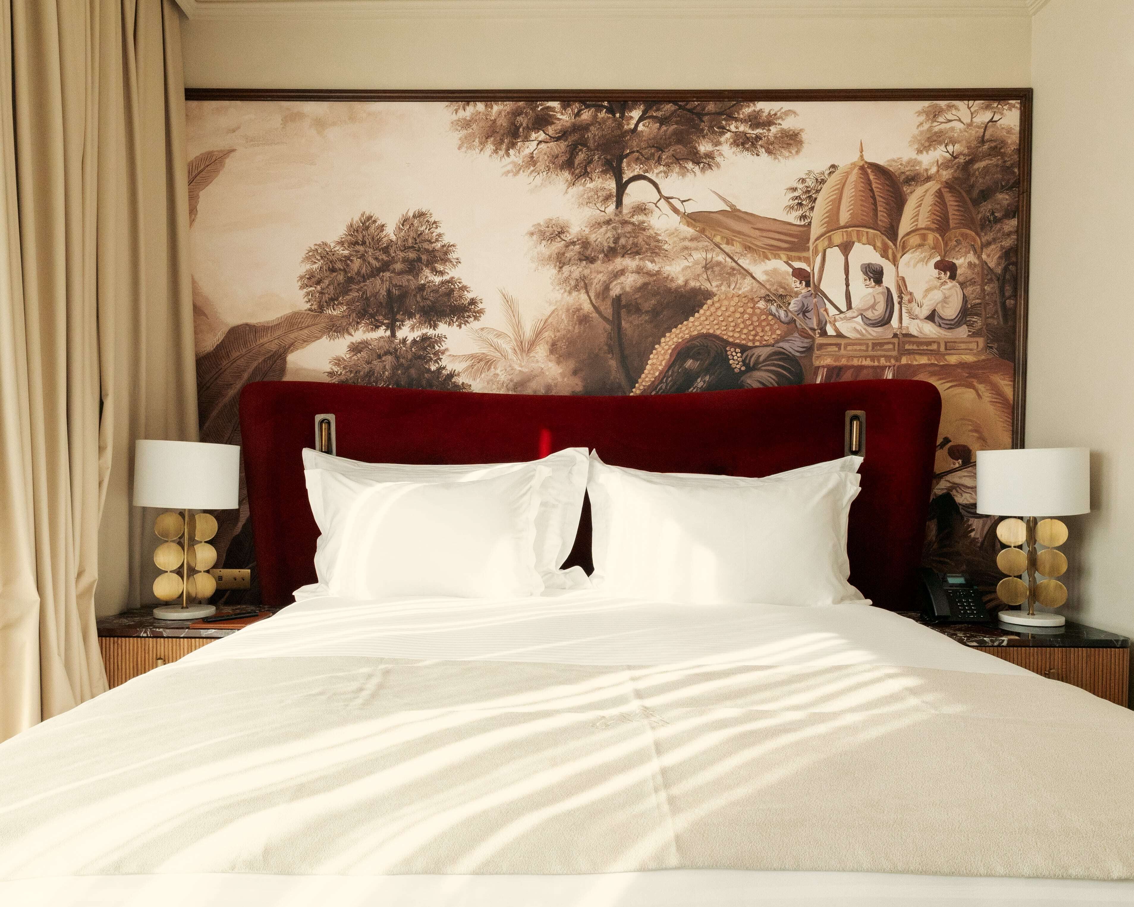 Une chambre d’hôtel avec un grand lit, une tête de lit, deux tables de chevet avec des lampes et un grand tableau au mur.