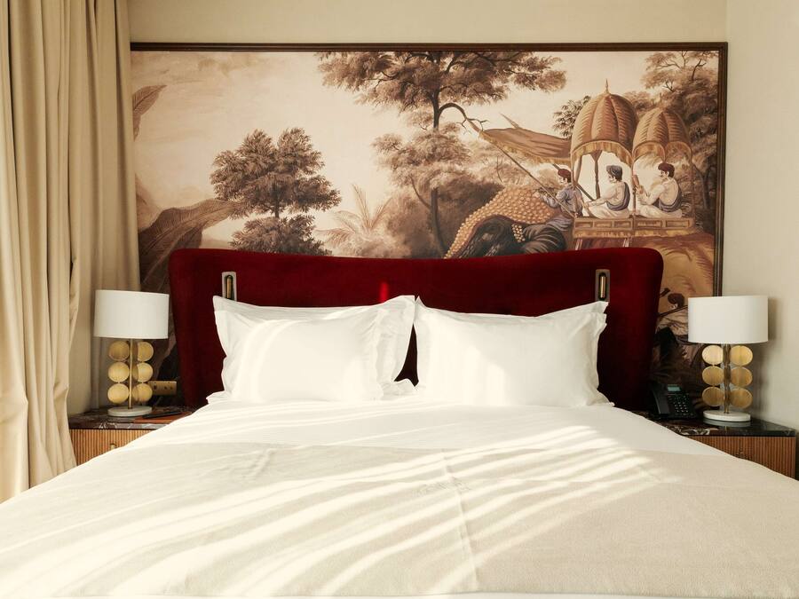 A hotel room with a large bed, a headboard, two bedside tables with lamps, and a large painting on the wall.