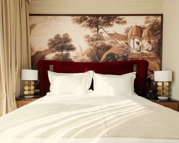 A hotel room with a large bed, a headboard, two bedside tables with lamps, and a large painting on the wall.