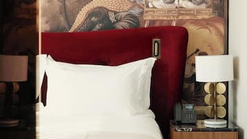 A hotel room with a large bed, a red headboard, a nightstand with a lamp, and a wall painting.