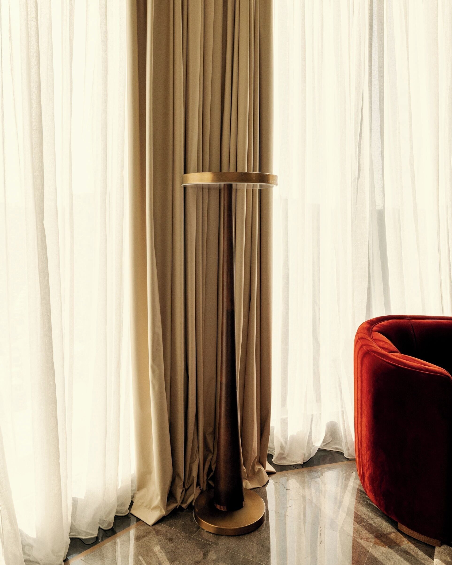 Une pièce avec un lampadaire, un fauteuil rouge et des rideaux transparents.
