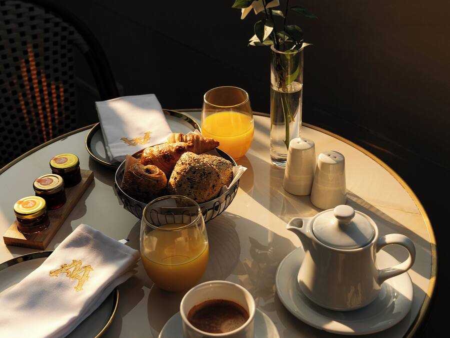 A breakfast table with croissants, muffins, a glass of orange juice, a cup of coffee, salt and pepper shakers, and a teapot.