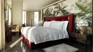 Habitación de hotel con una cama grande, un escritorio con silla, un teléfono y un cuadro con follaje tropical en la pared.