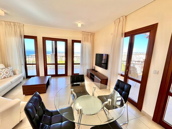 A modern living room with a glass coffee table, leather sofas, and a TV. - Perfect Getaway for 2 With Shared Pool (Kouklia)