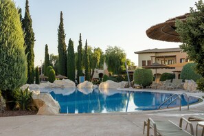 A swimming pool with a clear blue water, surrounded by rocks and trees, and a building with a tiled roof in the background. - Perfect Getaway for 2 With Shared Pool (Kouklia)
