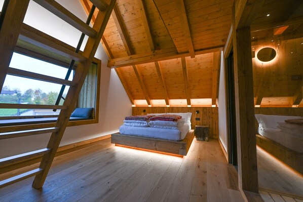 A loft-style bedroom with a wooden ceiling, a bed with pillows, a window, and a circular light fixture.