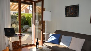 Een kamer met een laptop op een tafel, een fles wijn, glazen, een bank met kussens, een lamp en een ingelijst beeld aan de muur.