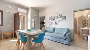 A modern living room with a light blue sofa, a dining table with chairs, and a kitchen area visible in the background. - 4215 Villa I Doni Della Luna by Barbarhouse (Porto Cesareo)