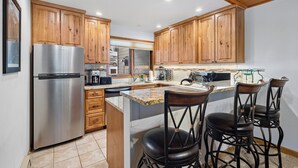 Una cocina con armarios de madera, un refrigerador de acero inoxidable, una encimera de granito y una zona con taburetes de bar.