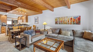 Un salón espacioso con techo de madera, una mesa de comedor con sillas, un conjunto de sofás y un cuadro en la pared.