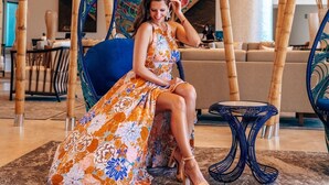 A woman seated on a blue chair with a peacock design, in a room with bamboo columns and a modern chandelier.