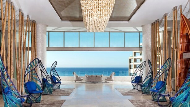 A modern lounge with hanging chairs, a bench, and a view of the ocean.