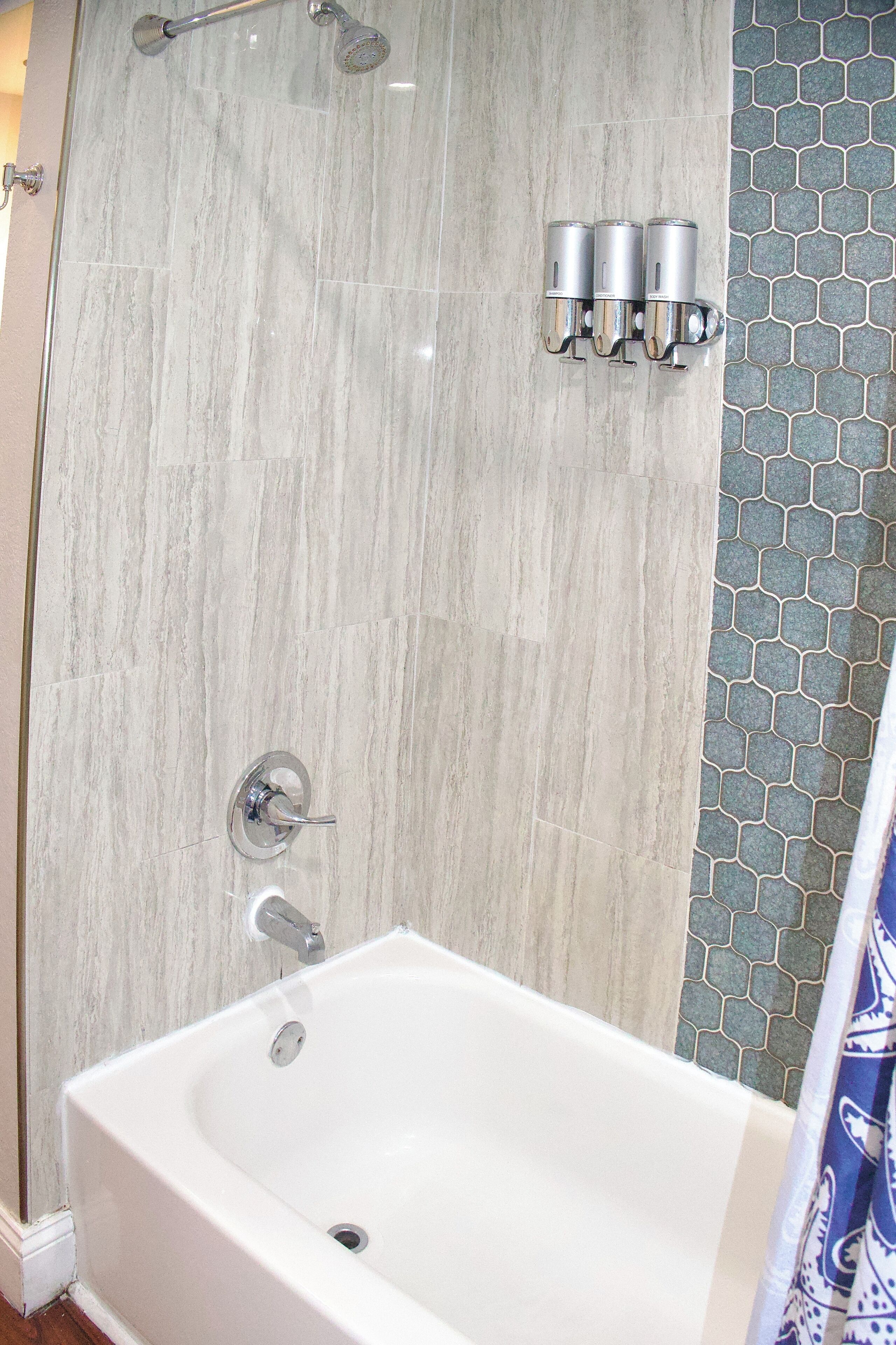 Un bagno con una vasca da bagno bianca, una doccia con porta in vetro e un rivestimento a parete con motivo esagonale.