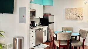 Una cocina compacta con microondas, cafetera y refrigerador. Hay un área de comedor con una mesa y sillas.