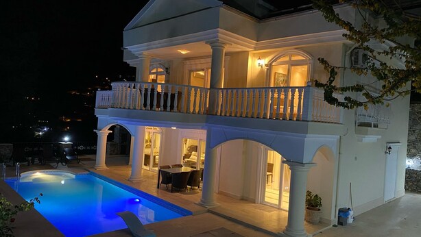 Une maison à deux étages avec une piscine, un espace salon extérieur et un balcon.