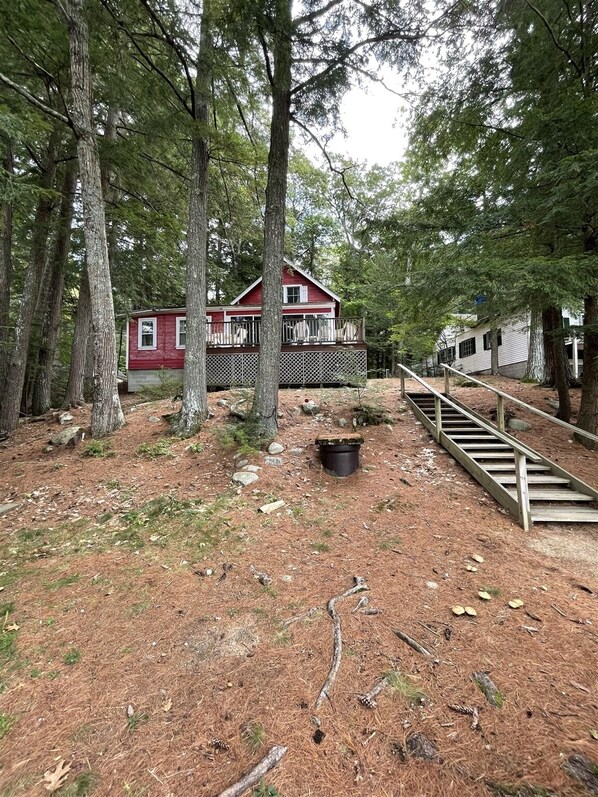 A cabin surrounded by tall trees, a wooden deck, and a staircase leading up to the house.