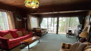 Interior acollidor d'una cabana amb sostre de fusta, un sofà vermell, un sofà escocès i una taula de centre de fusta.