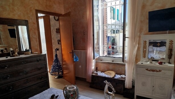 Una stanza con un comò in legno, un piccolo abete decorato, un tavolo con tovaglia all'uncinetto e una finestra con inferriate.