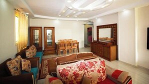 Una sala de estar con un sofá, una mesa de comedor con sillas, un aparador de madera y un espejo grande en la pared.