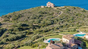 Una proprietà costiera con piscina, un edificio grande e un paesaggio collinare.