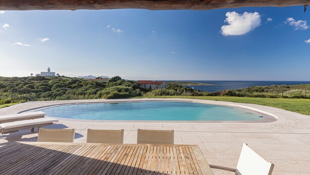 Una piscina con lettini e un tavolo, immersa nel verde e con vista sul mare.