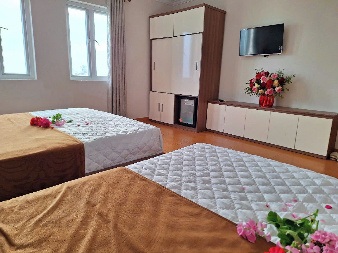A hotel room with two beds, a TV, a minibar, and a flower vase.