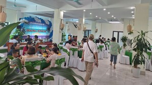 A spacious indoor dining area with tables set for guests, ceiling fans, and a stage with a backdrop. - Green Co to Hotel (Co To)