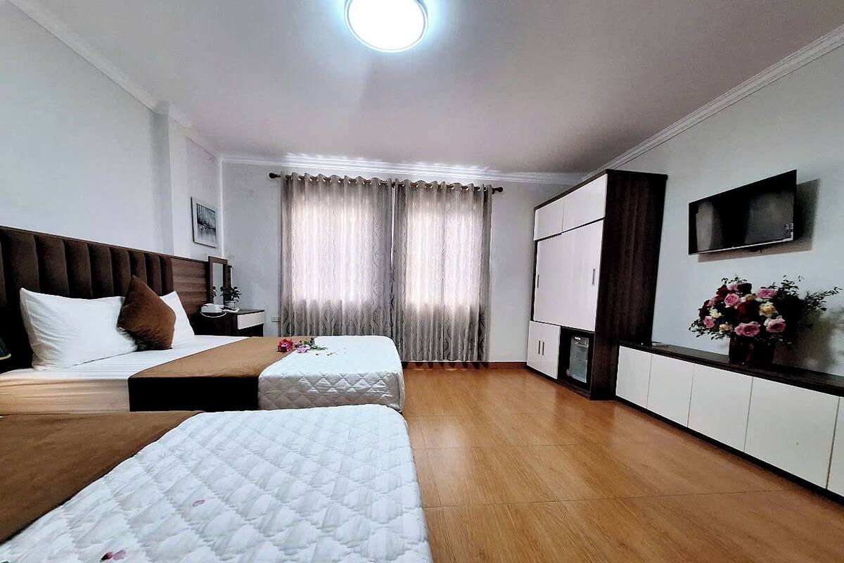 A hotel room with two beds, a TV, a desk, and a cabinet.