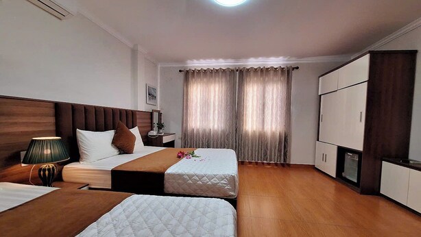 A hotel room with two beds, a wooden floor, a large window with curtains, a ceiling light, and a wardrobe. - Green Co to Hotel (Co To)