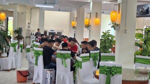A banquet hall with round tables, white chairs with green sashes, and overhead lighting. - Green Co to Hotel (Co To)