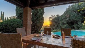 Un espace extérieur aménagé pour prendre les repas, avec vue sur une piscine et sur le coucher de soleil.