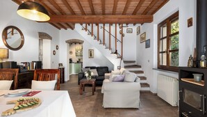 Un vaste espace de vie comprenant un escalier, une table à manger dressée avec de l’argenterie et un plateau de concombres, ainsi qu’un coin salon confortable avec un canapé et des fauteuils.