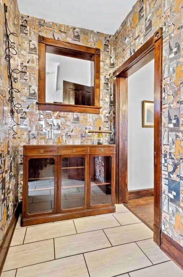 A room with a tiled floor, a wooden cabinet with glass doors, and a mirror above it. The walls are covered with a collage of images. - Stay in a Historic Charm in the Heart of Lexington (Lexington)
