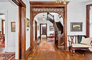 A grand entryway with a wooden archway, a staircase, and a seating area with a bench and cushions. - Stay in a Historic Charm in the Heart of Lexington (Lexington)