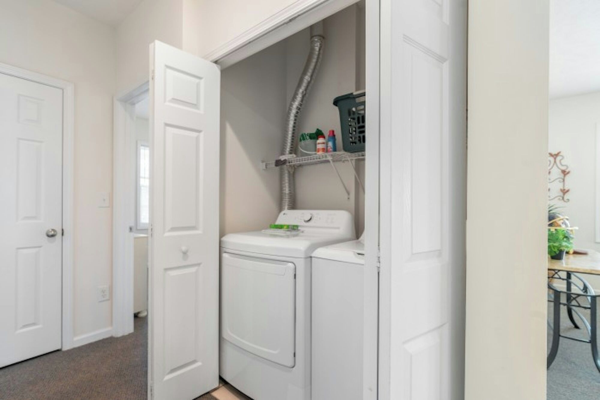 Une buanderie équipée d’un lave-linge et d’un sèche-linge, d’une étagère contenant des produits de nettoyage et d’une porte donnant sur une autre pièce.