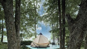 A hammock set up between two trees, a tent, and a table with chairs in a wooded area. - KANALIAN HOTEL (Nagawa)