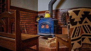 A room with a blue wood-burning stove, a wooden chair, a brick fireplace, and a patterned throw blanket. - KANALIAN HOTEL (Nagawa)