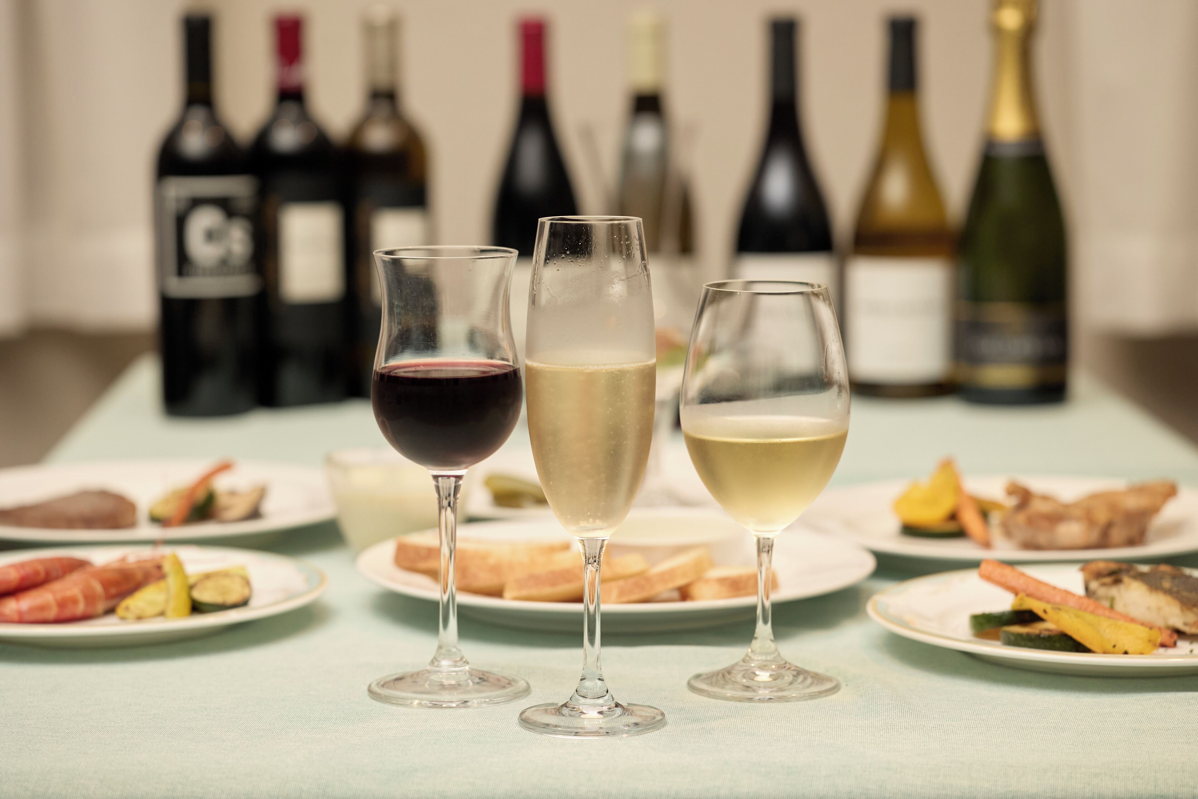 A table with three glasses of wine and plates of food.