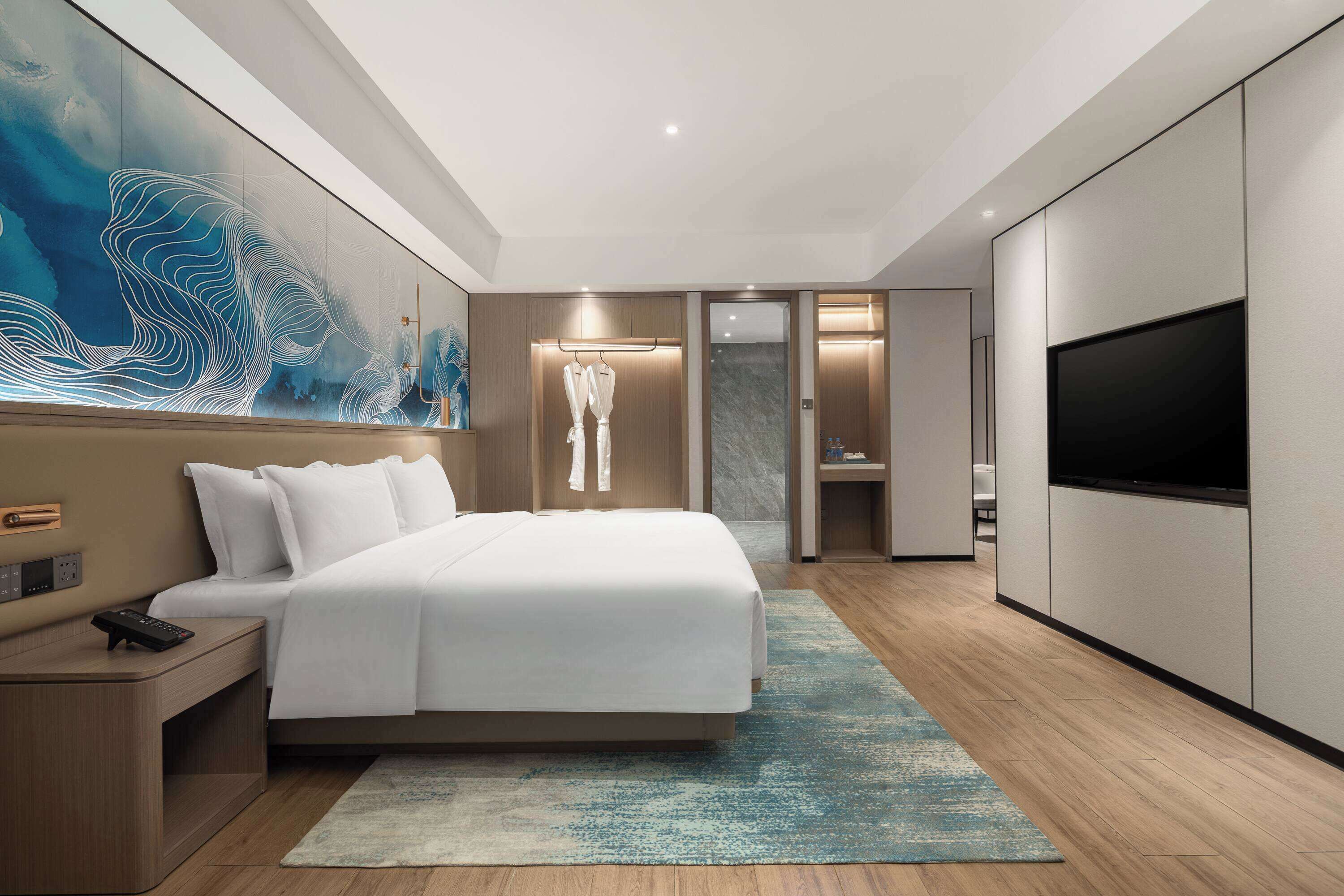 A modern hotel room with a large bed, a TV, and a bathroom visible through an open door.
