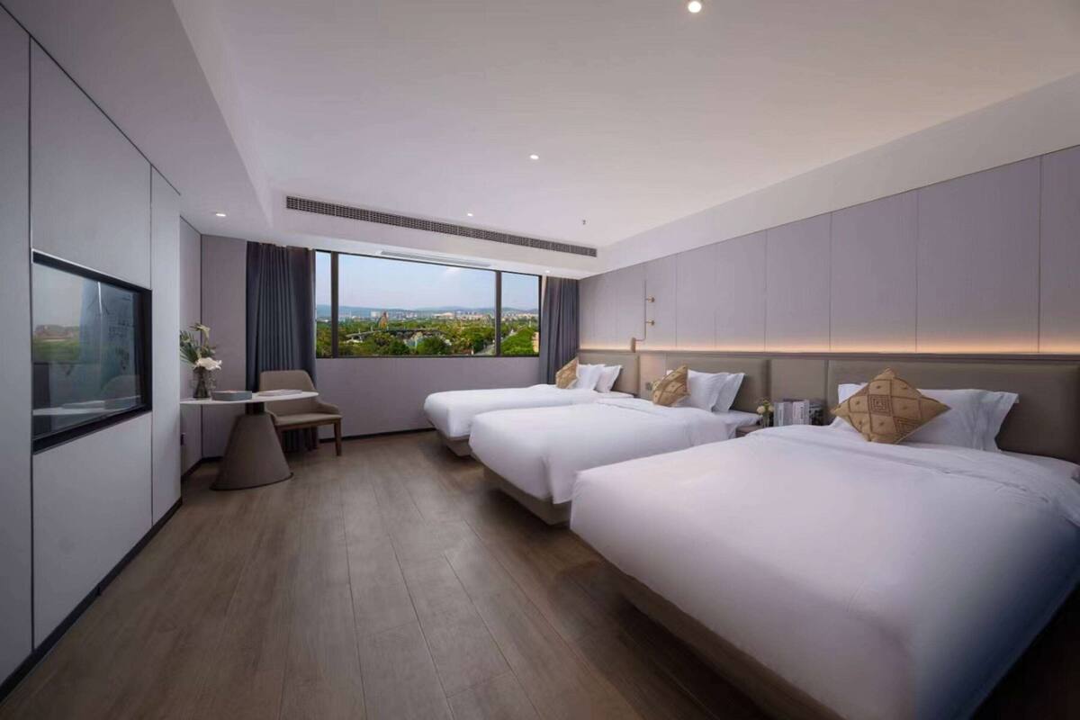 A modern hotel room with two beds, a desk, and a large window offering a city view.