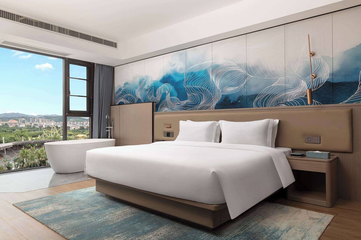 A modern hotel room with a large bed, a view of the city, and a unique wall mural.