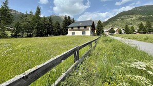 Una casa con balcón, rodeada por un campo cubierto de hierba y montañas.