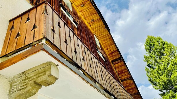 Un edificio con fachada de madera, un balcón con barandillas de metal y un cielo despejado al fondo.