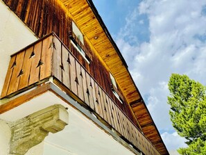 Un edificio con fachada de madera, un balcón con barandillas de metal y un cielo despejado al fondo.